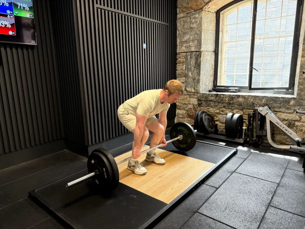 Fitness coach Scott Laidler performing a barbell deadlift in a professional gym setting, demonstrating evidence-based strength training